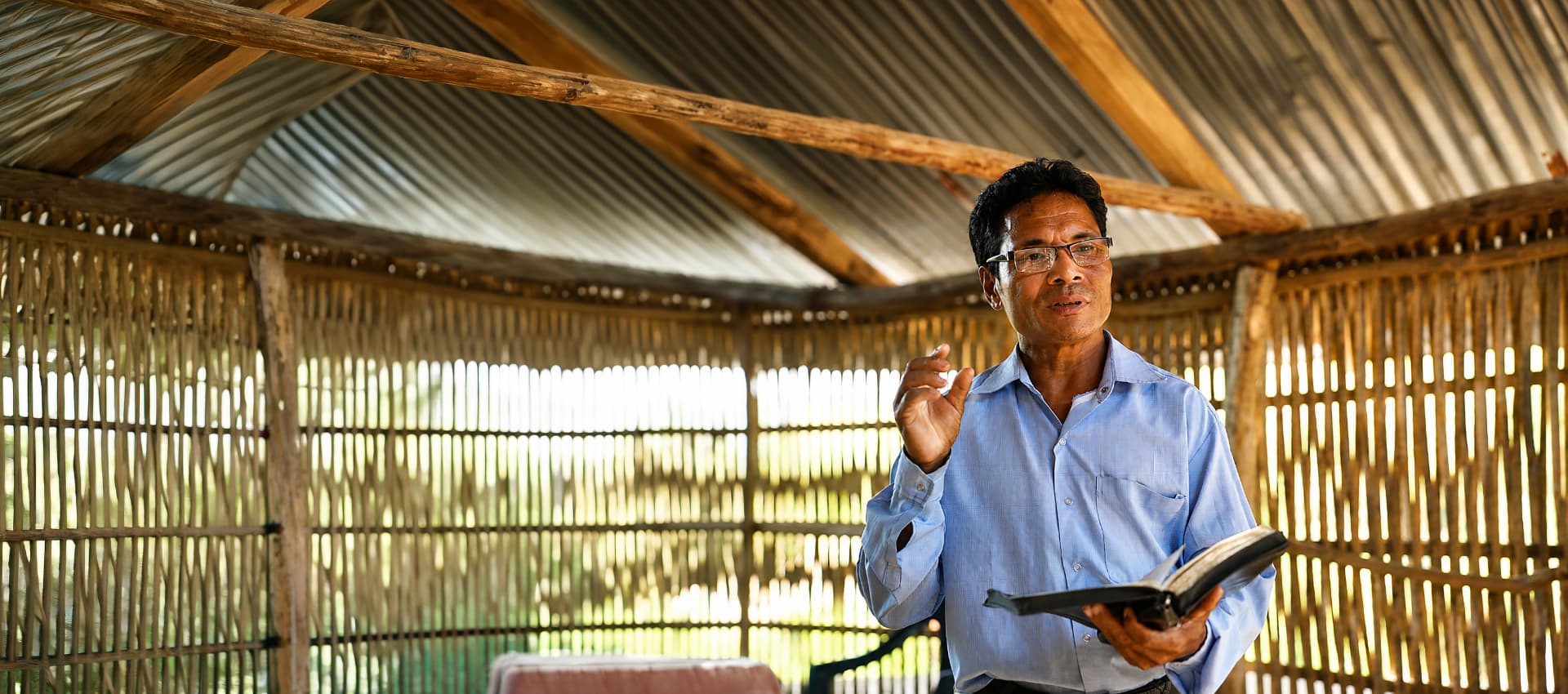 A Bible worker preaching from an open Bible in a bamboo chapel