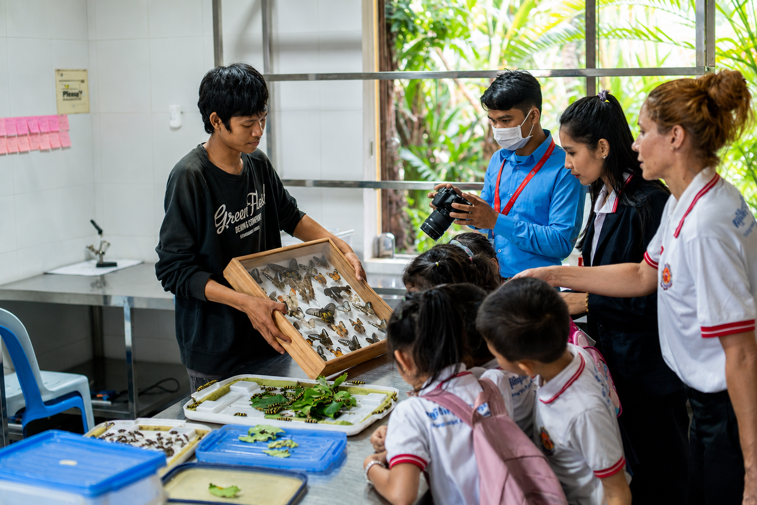 Students and teachers gathered around a display of butterflies and caterpillars in an Asian classroom